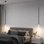 A modern minimalist bedroom with a gray bed, dark and light bedding, two white nightstands, decorative items, and slim pendant lights hanging from the ceiling, casting a soft pendant light downward.