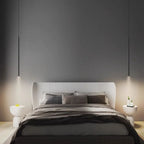 A modern bedroom features a large bed with gray and beige bedding, flanked by two white nightstands. A pendant light hangs above each nightstand, adding sleek illumination against the solid dark gray wall behind the bed.