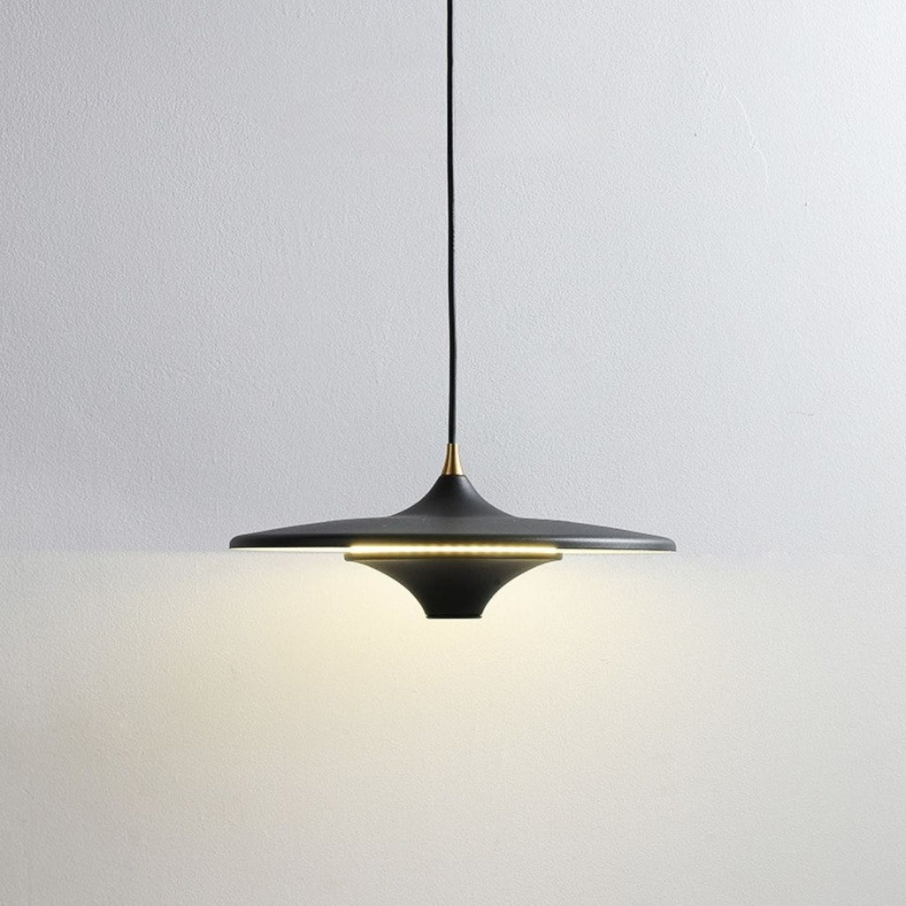 A modern black pendant light with a wide, flat shade hangs from the ceiling, casting a soft, warm glow on a plain white wall.