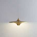 A modern, gold pendant light with a wide, flat shade hangs from a white cord against a plain, light-colored wall, casting a soft, even glow below it.