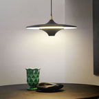 A modern black pendant light hangs above a table with a green geometric vase and a dark, oval-shaped dish, casting soft light onto the surface.