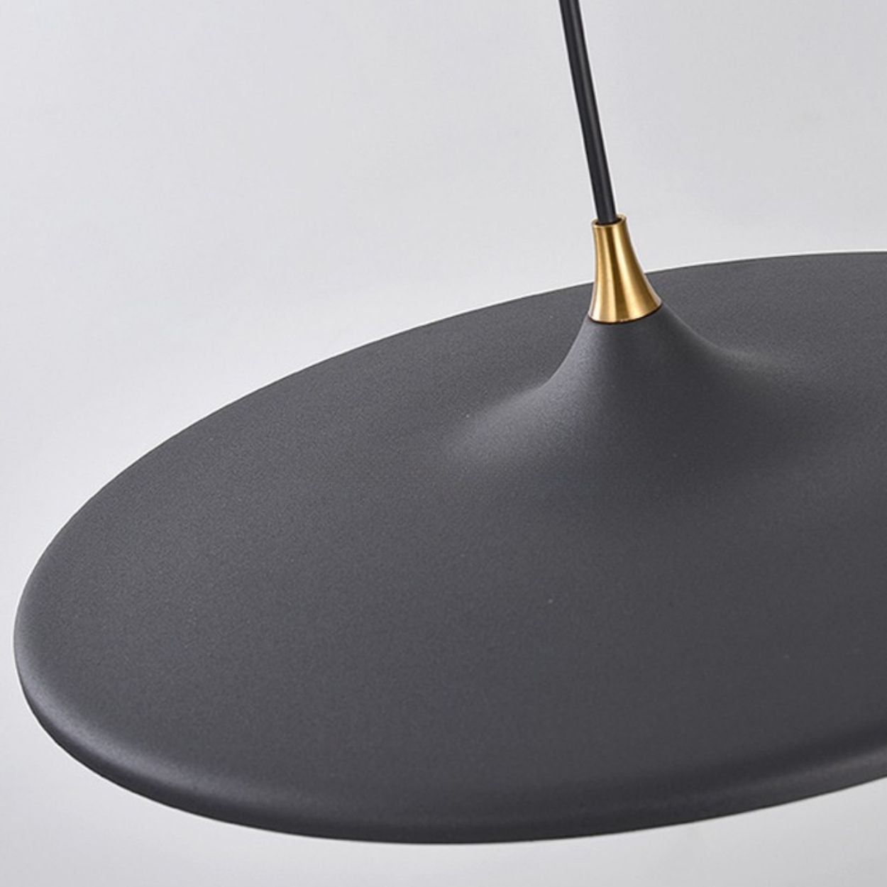 A close-up of a modern pendant light features a smooth, matte black shade and a gold accent near the top, hanging from a black cord against a plain light background.