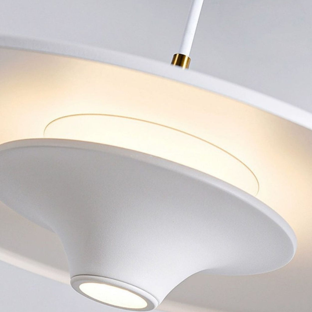 Close-up of a modern white pendant light with smooth, curved surfaces and a glowing circular center, casting a soft, warm light. The fixture hangs from a white cord with a gold accent for added elegance.