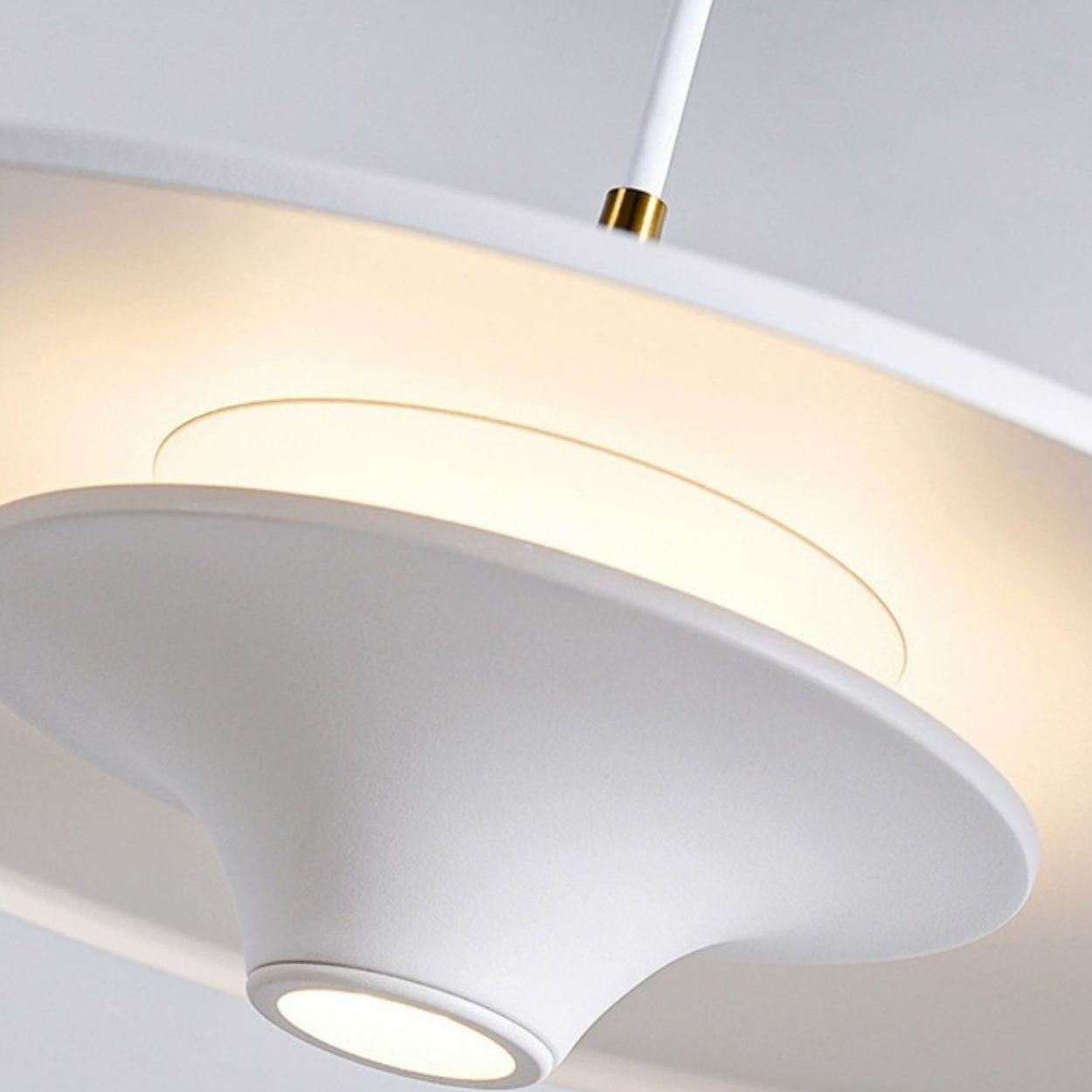 Close-up of a modern white pendant light with smooth, curved surfaces and a glowing circular center, casting a soft, warm light. The fixture hangs from a white cord with a gold accent for added elegance.