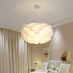 A modern bedroom features a large, white pendant light with a wavy design hanging from the ceiling, beige walls, plush toys on the bed, light curtains, and a small framed picture above the bed for a cozy touch.