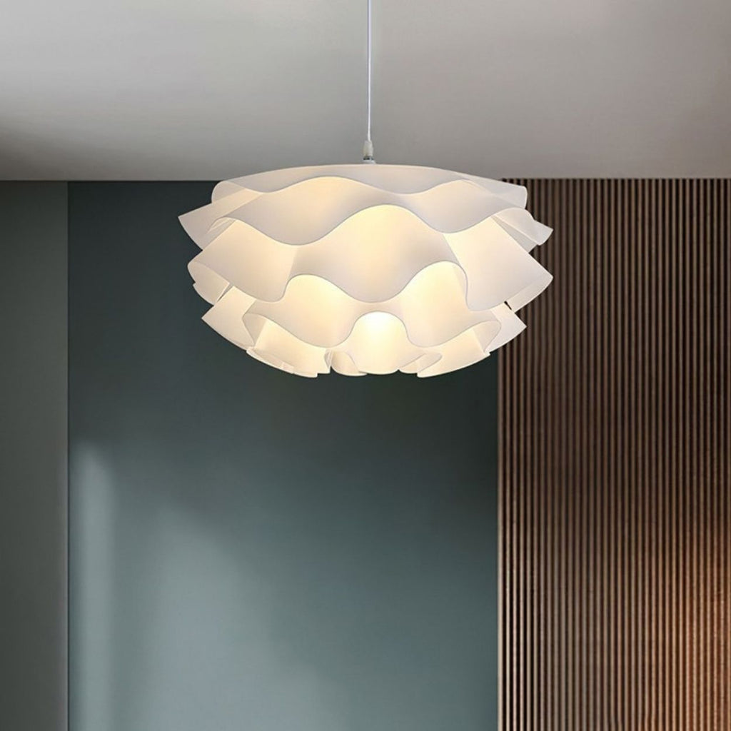 A modern pendant light with a wavy, layered white shade hangs from the ceiling. The background features a green wall and a section of vertical wooden slats.