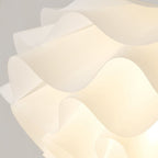 Pendant Light Close Up: A modern, white, sculptural lampshade with wavy, overlapping, translucent panels is softly illuminated from within.