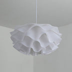 A modern pendant light with a wavy, ruffled white lampshade hangs from the ceiling in a minimalist room with light-colored walls.