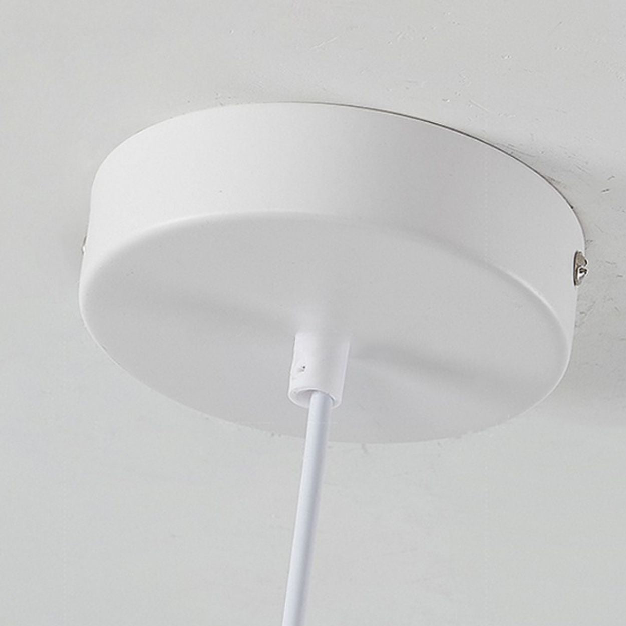 A close-up view of a round, white pendant light mount canopy with a white cord hanging down from its center, mounted on a white ceiling.