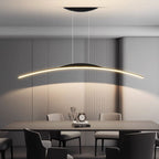 A modern dining room with a long rectangular table, surrounded by six chairs, features a sleek pendant light hanging above. Soft lighting from the pendant light creates a minimalist and elegant atmosphere. An abstract sculpture and clock sit on the table.