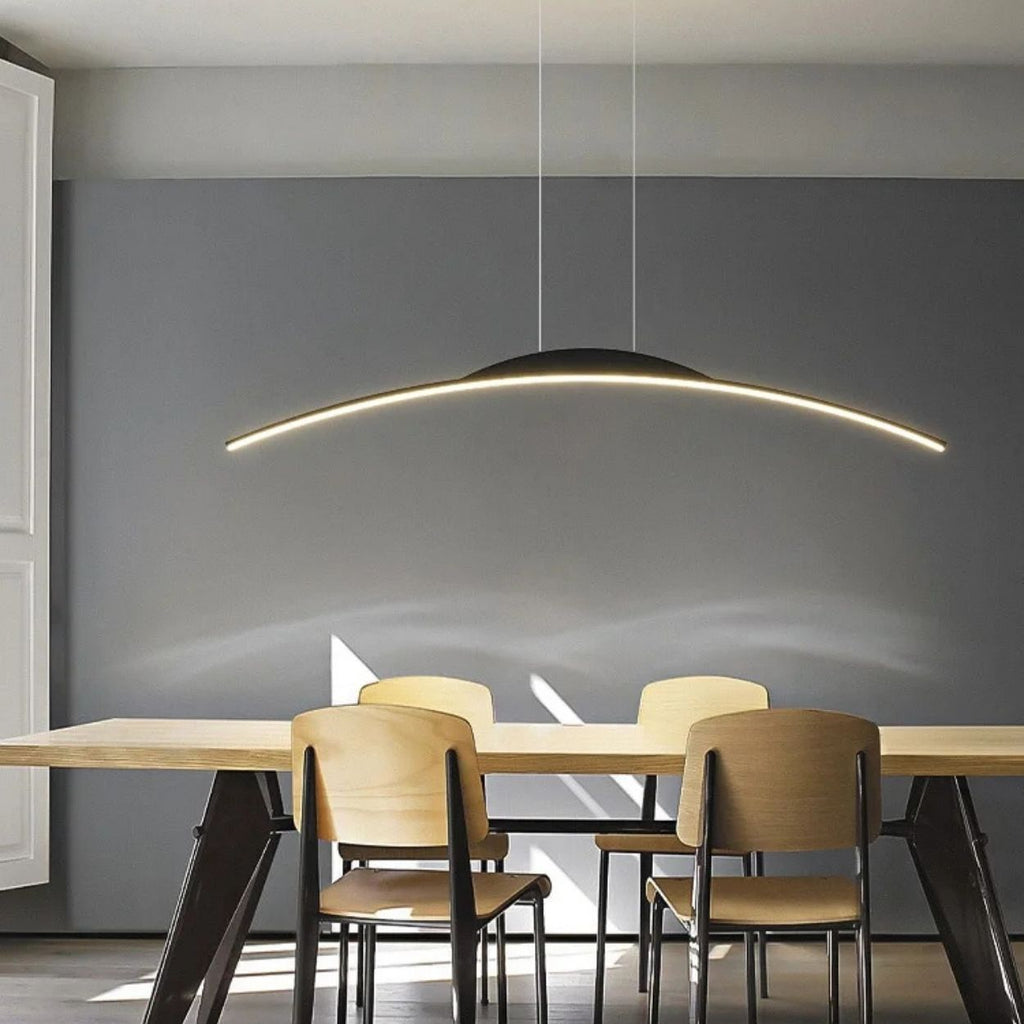 A modern dining room with a wooden table, four light wooden chairs, a dark gray accent wall, and a sleek pendant light illuminating the space from above.