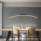 A modern dining room with a wooden table, four light wooden chairs, a dark gray accent wall, and a sleek pendant light illuminating the space from above.