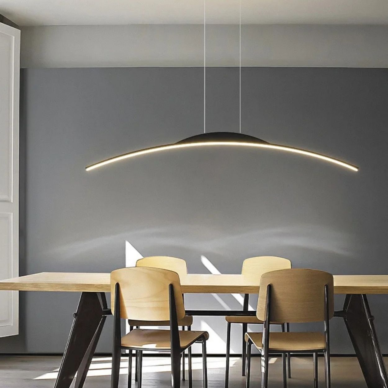 A modern dining room with a wooden table, four light wooden chairs, a dark gray accent wall, and a sleek pendant light illuminating the space from above.