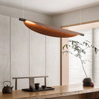 A modern dining area with a wooden table set for tea, a minimalist wood and metal chandelier overhead, and a simple potted plant against light-colored paneled walls.