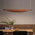 A modern dining room with a wooden table set for two, featuring a centerpiece with oranges and branches in a vase, and a large, curved wooden chandelier hanging above.