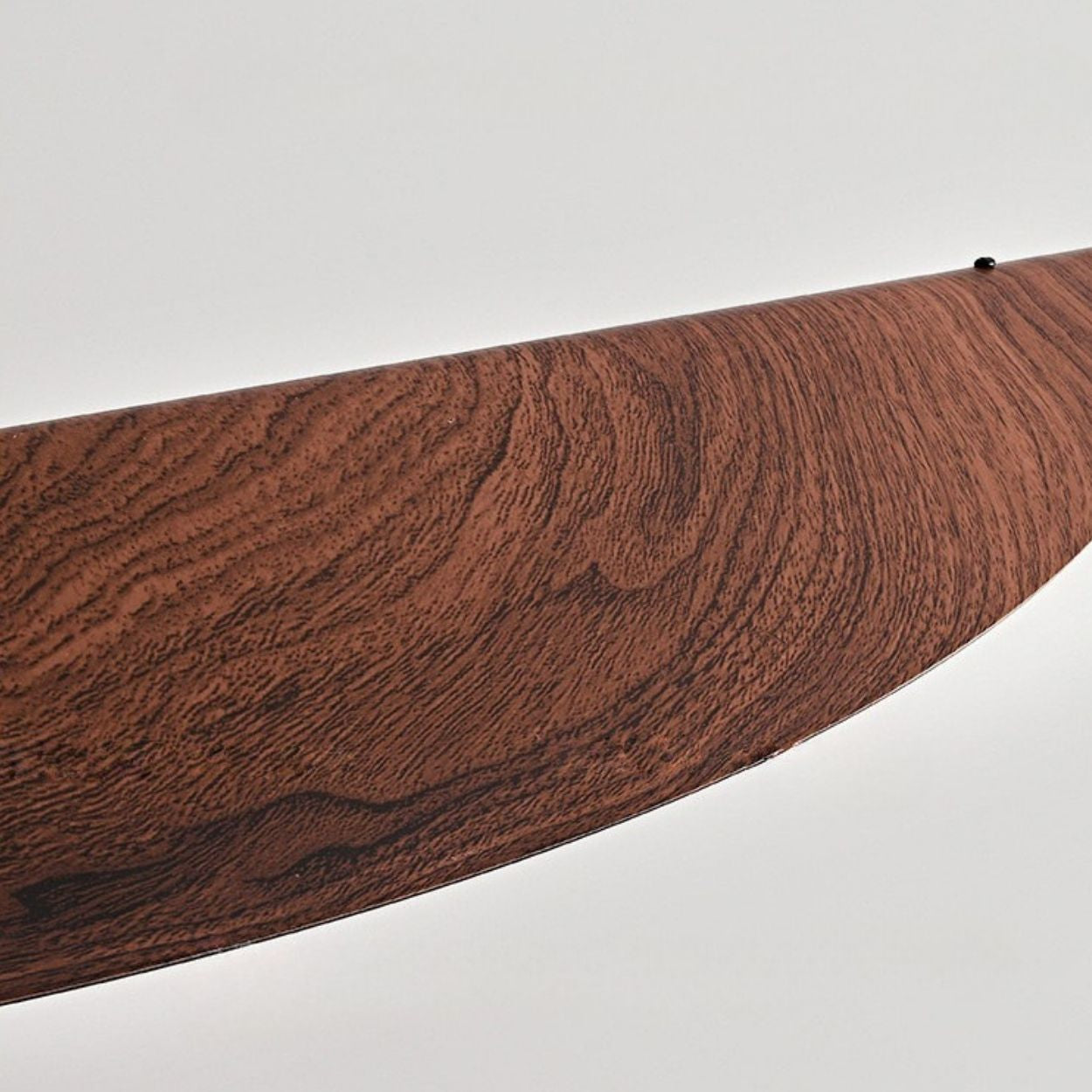 A close-up of a curved object with a wood grain texture against a plain, light background. The smooth, polished surface hints at an elegant chandelier close up, possibly part of a unique piece of furniture or an art installation.