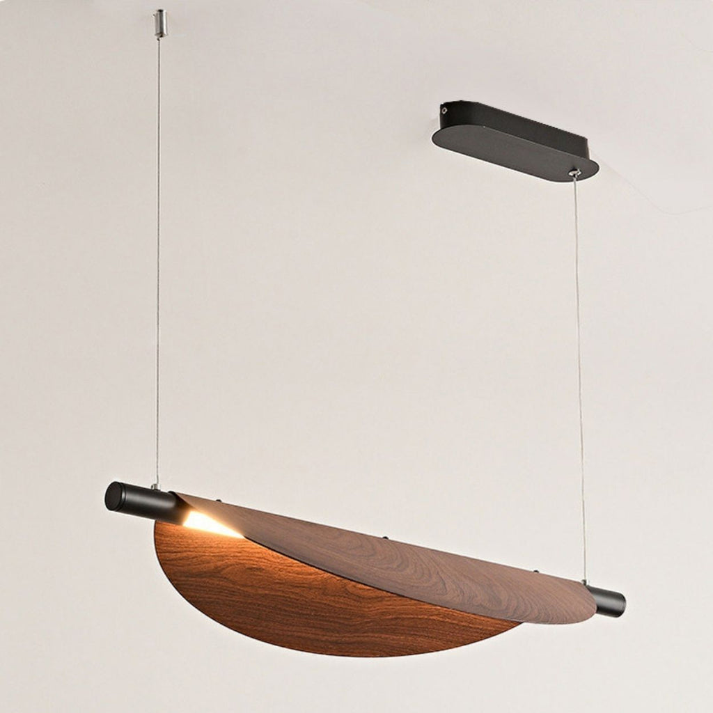 A modern chandelier pendant light with a curved wooden shade and black metal accents, suspended from the ceiling by two thin wires, emits light elegantly from one end.