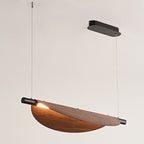 A modern chandelier pendant light with a curved wooden shade and black metal accents, suspended from the ceiling by two thin wires, emits light elegantly from one end.