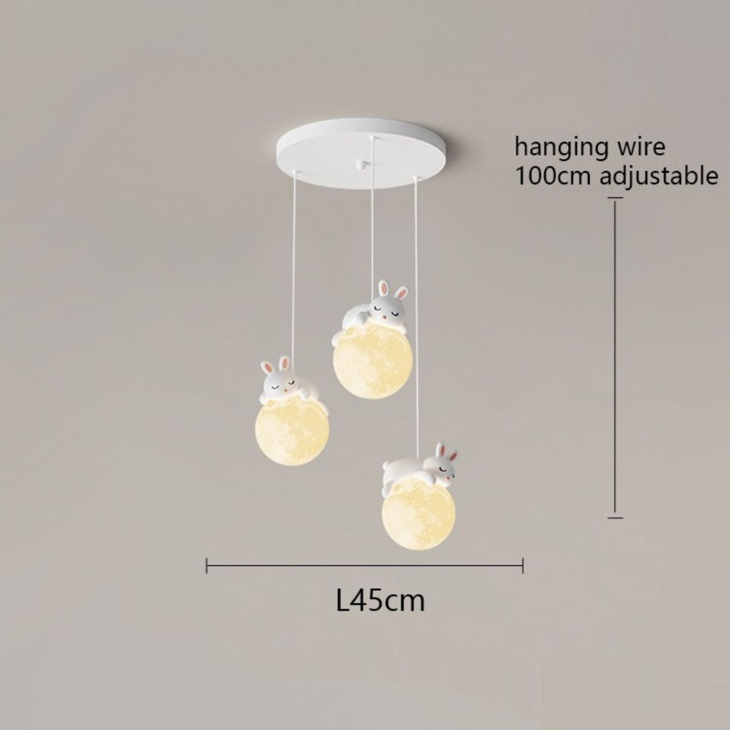 A charming pendant light fixture with three hanging bunny-shaped lights, each perched on a glowing orb. Adjustable cords extend up to 100 cm, and the fixture spans 45 cm wide. Perfect for adding whimsy to any space against a neutral background.