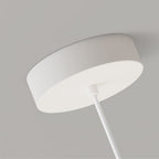 A close-up view of a minimalist white pendant light mount with a round base attached to the ceiling and a rod extending downward.
