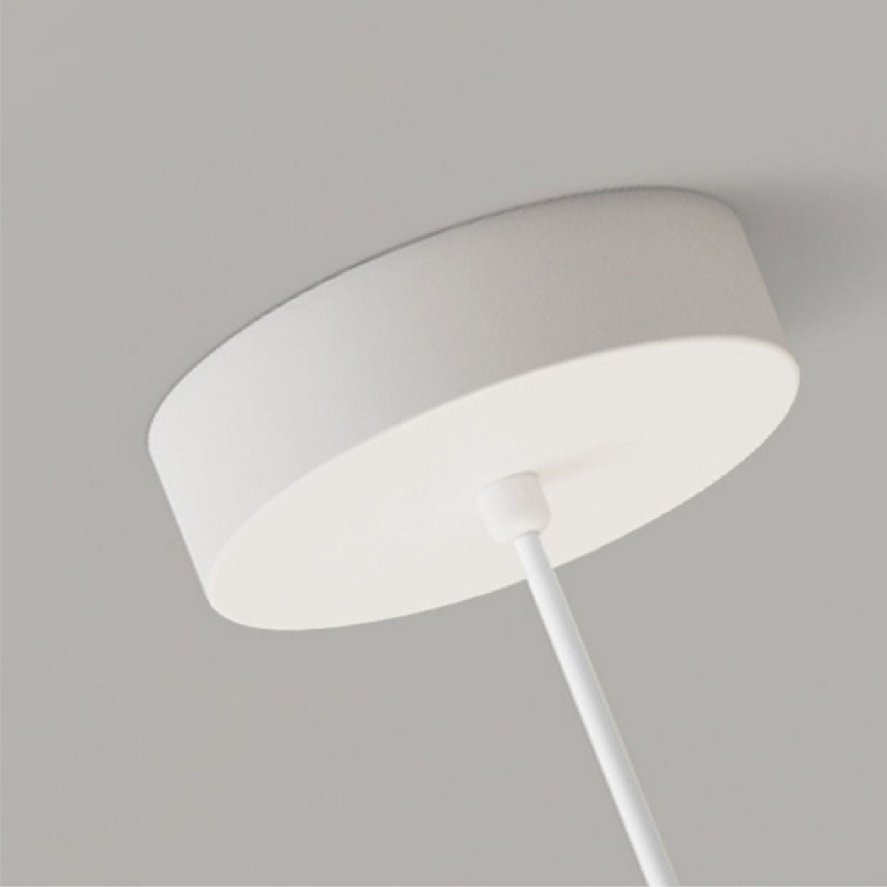 A close-up view of a minimalist white pendant light mount with a round base attached to the ceiling and a rod extending downward.
