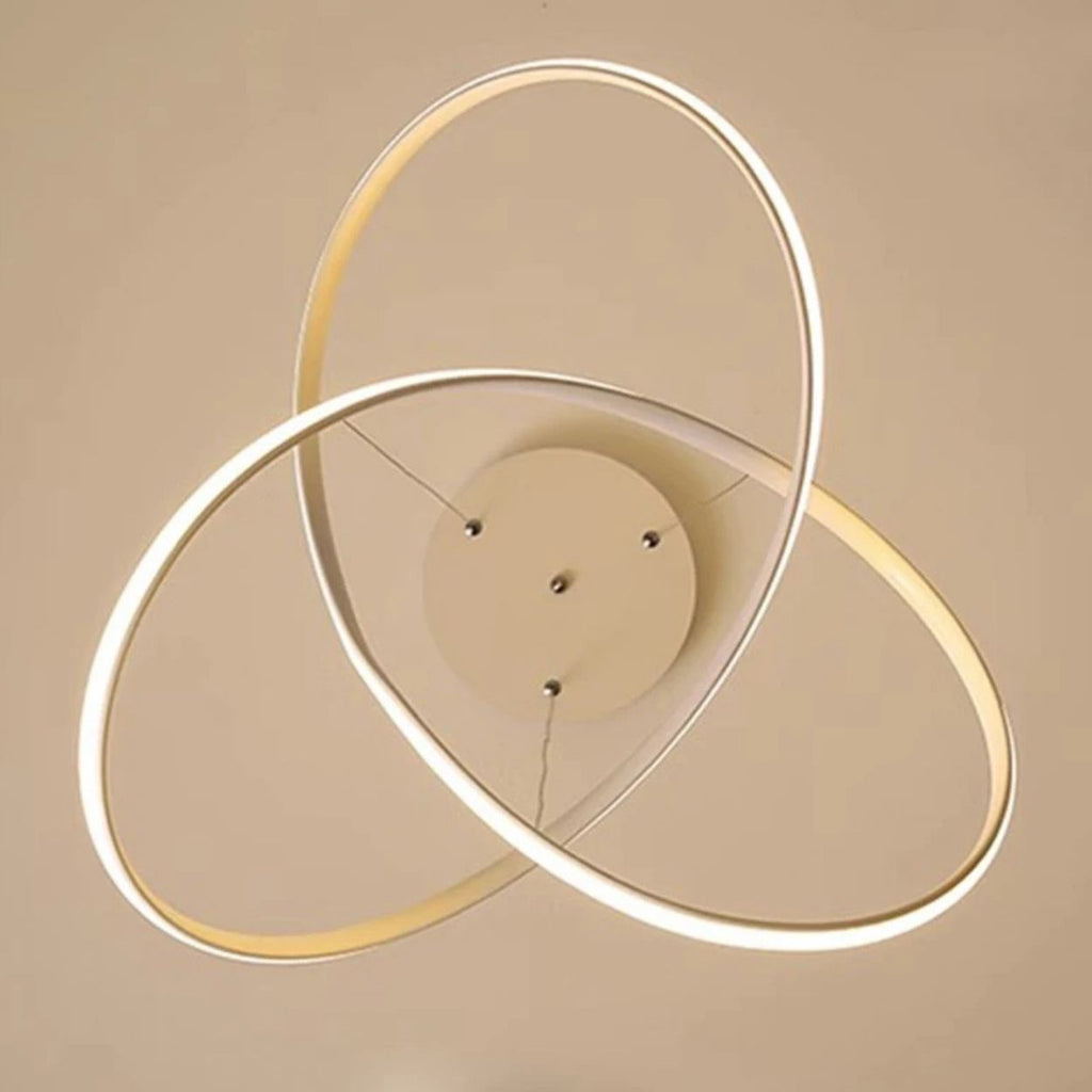 A modern pendant light fixture with three interlocking, glowing LED rings attached to a round central base, set against a beige ceiling.