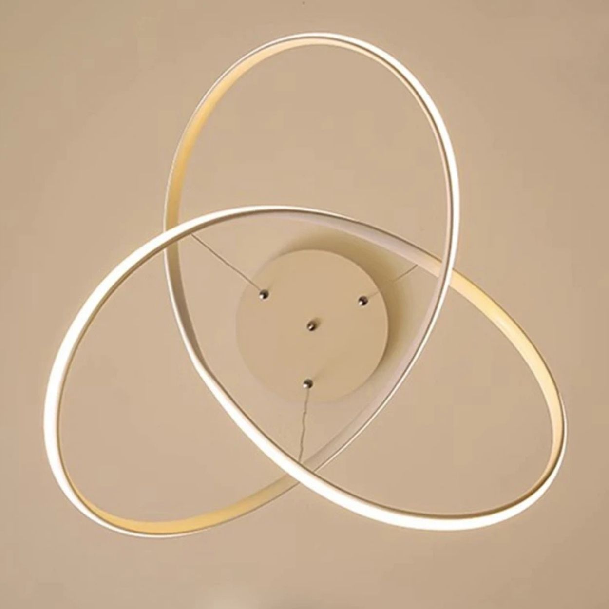 A modern pendant light fixture with three interlocking, glowing LED rings attached to a round central base, set against a beige ceiling.