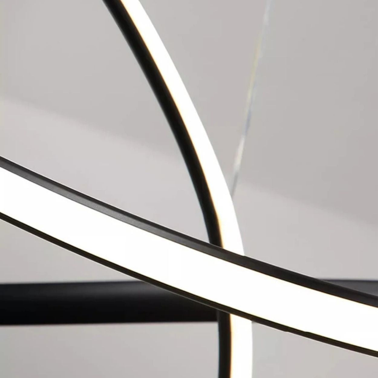 A close-up view of intersecting curved LED light strips against a neutral background, creating an abstract, modern pendant light close up with bright white illumination.