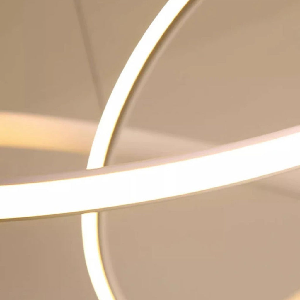Close-up of curved, glowing white LED light strips evokes the look of a pendant light close up against a soft beige background, creating an abstract and modern design with intersecting lines and gentle shadows.