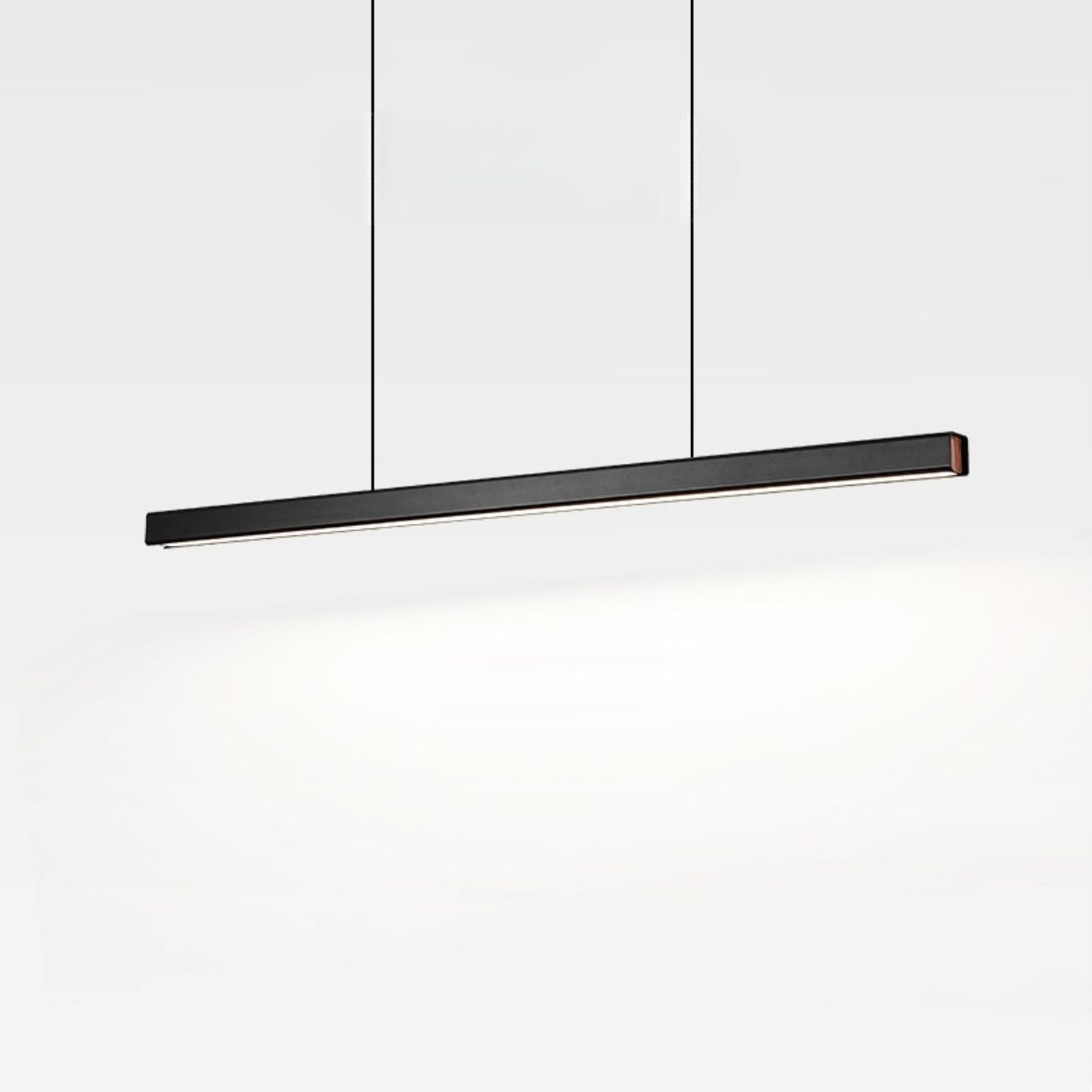 A modern, black pendant light hangs from the ceiling by two thin cords, illuminating a white background with a soft glow.