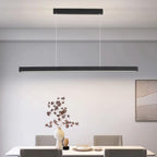 A modern dining room features a long, rectangular pendant light hanging above a white table set with a decorative vase, plates, and four chairs. A minimalist framed artwork adorns the wall.
