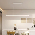 A modern dining room with a rectangular white table, three unique chairs in grey, yellow, and cream, minimalist decor, wall art, and a striking pendant light illuminating the space from above.