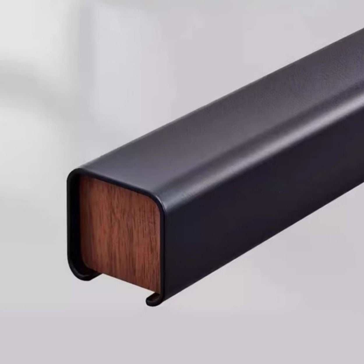 A close-up of a rectangular pendant light with a wooden center, encased in a smooth, matte black metal cover, set against a neutral background.
