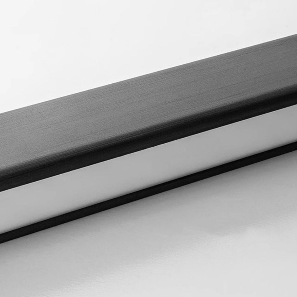 A close-up view of a rectangular object with a black top and white side, possibly a minimalist desk organizer or box, placed on a white surface. The grayscale image evokes the clean lines of a pendant light close up.
